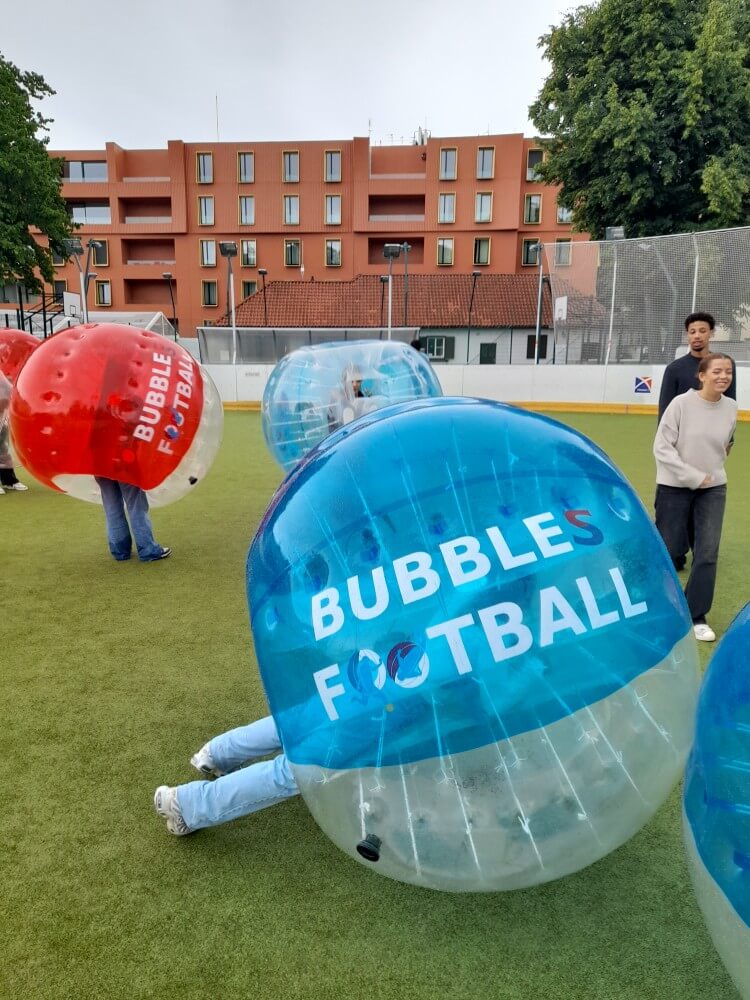 Gruppenteilnehmer spielen Bubble Football in bunten, durchsichtigen Kugeln auf einem Sportplatz.