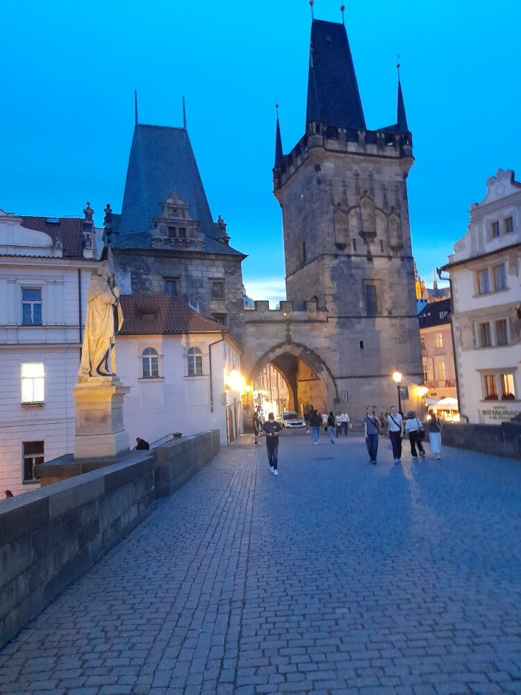 Die Karlsbrücke in Prag erleuchtet von warmem Licht, während Besucher den historischen Torbogen passieren.