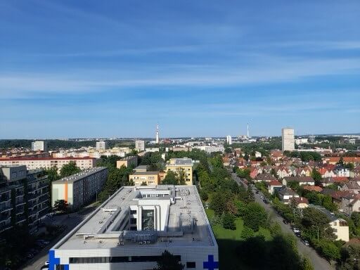 Blick über die Stadt mit modernen Gebäuden und grünen Flächen unter einem klaren blauen Himmel.