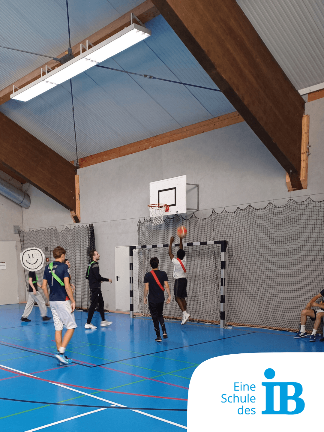Schüler spielen Basketball in der Sporthalle einer Schule des IB, während einer einen Korb wirft.